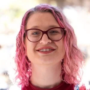 Woman with pink hair smiling outdoors.