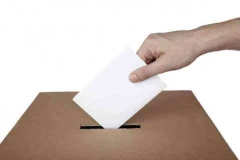 Hand casting vote into ballot box, democracy concept.