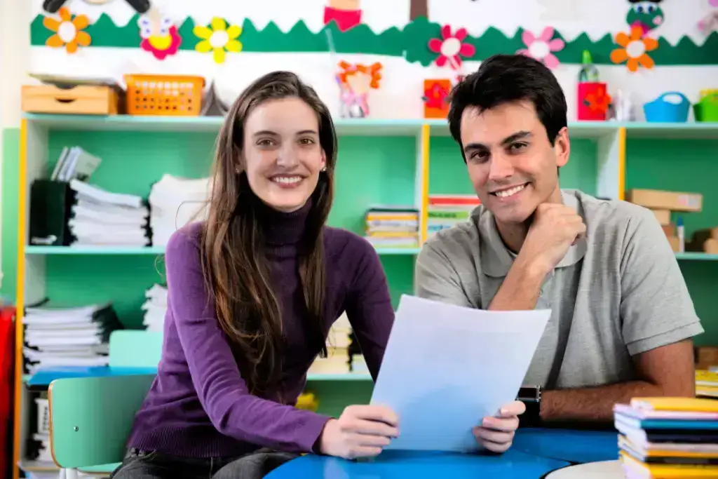 Teachers smiling in colourful classroom setting.
