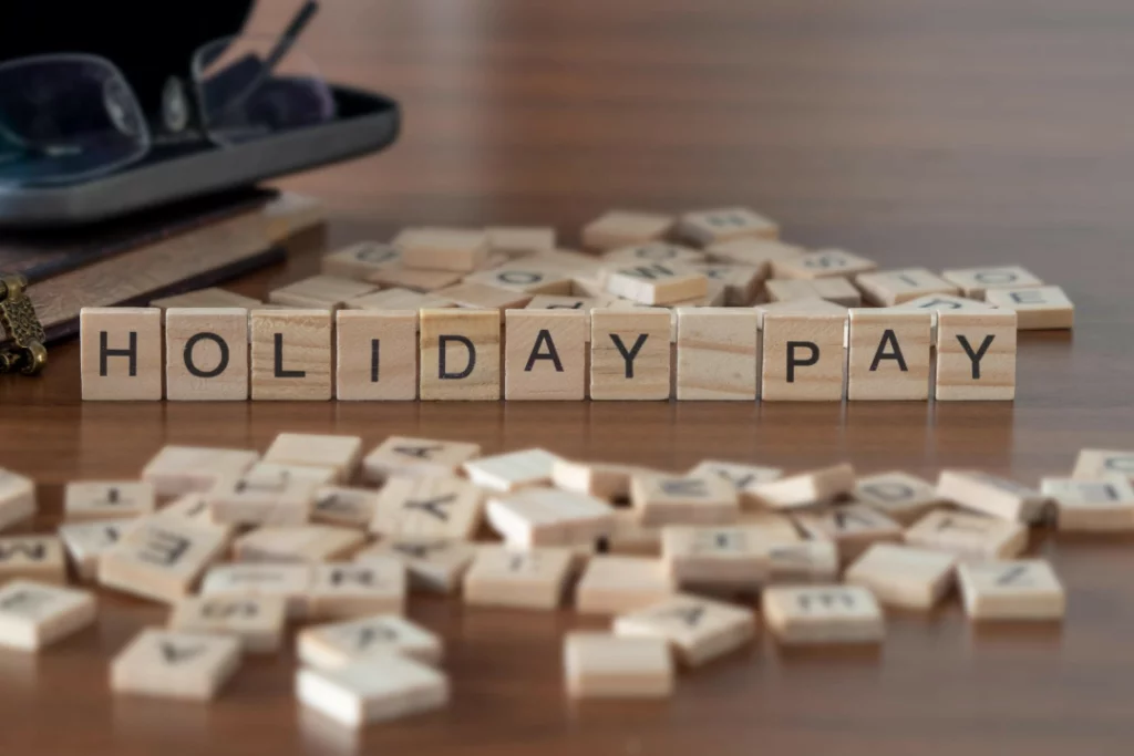 Wooden blocks spelling "holiday pay" on table.