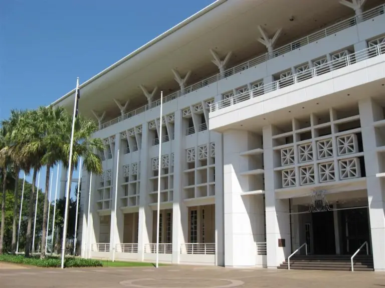 Modern white civic building with palm trees and flagpoles