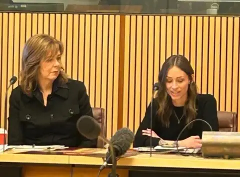 Two women seated at a formal hearing table