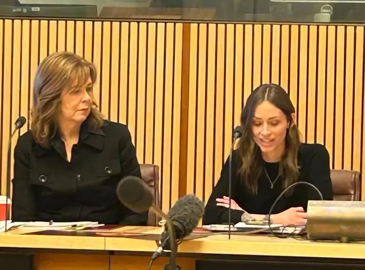 Two women seated at a formal hearing table